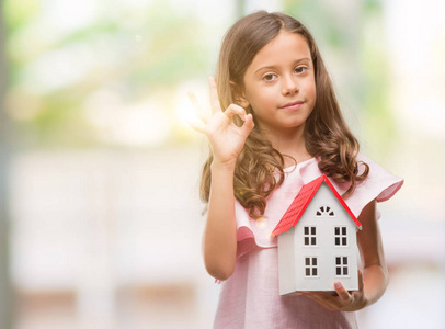 深色头发的西班牙裔女孩，抱着小房子，用手指做OK标志，非常好的象征