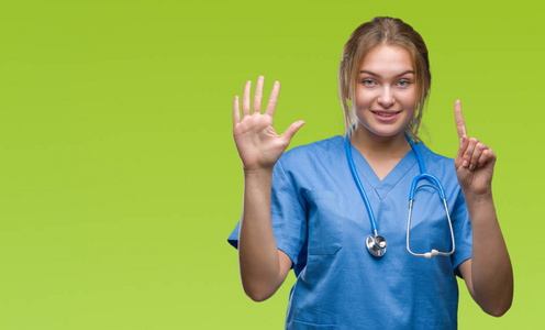 年轻的白种人医生女士穿着外科医生制服，在孤立的背景上显示和指着数字6，同时微笑自信和快乐。