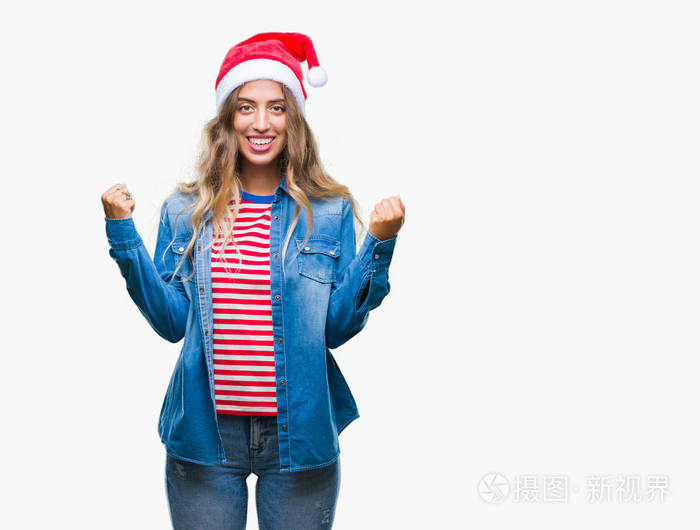 美丽的金发女郎戴着圣诞帽，在孤立的背景上庆祝，惊讶和惊讶的成功，举起手臂和睁开眼睛。 赢家概念。