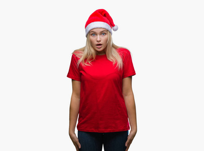 年轻的高加索女人戴着圣诞帽，在孤立的背景下害怕和震惊，惊讶的表情，恐惧和兴奋的脸。