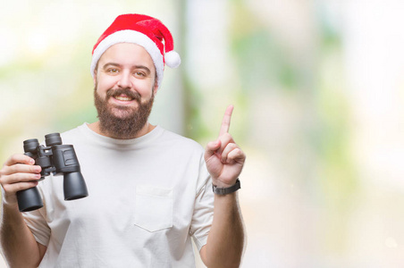 一个年轻的高加索人，戴着圣诞帽，在一个孤立的背景下用望远镜观察，惊讶地发现了一个想法或一个问题，他脸上露出了幸福的表情