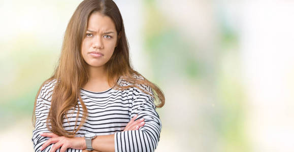 年轻漂亮的黑发女人穿着条纹毛衣，在孤立的背景怀疑和紧张的不赞成的表情在脸上交叉的手臂。 消极的人。