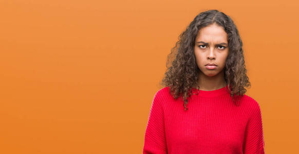 年轻的西班牙裔女人穿着红色毛衣，怀疑和紧张的皱眉，因为问题而心烦意乱。 消极的人。