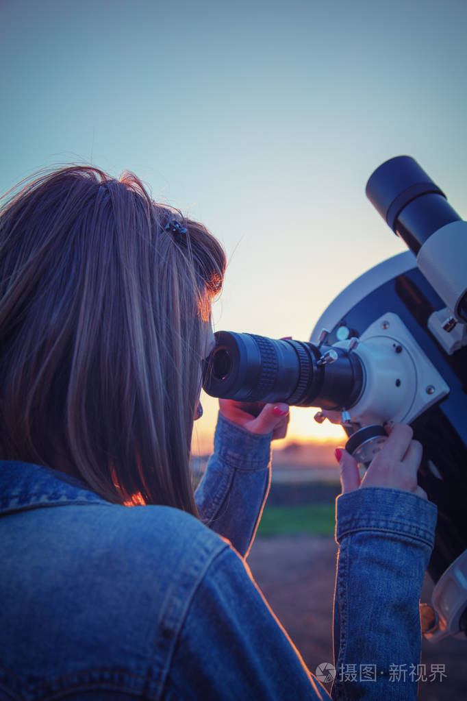 可爱的年轻女人拿着天文望远镜看着天空