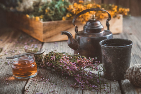 老式茶壶杯的健康草药茶，小蜂蜜罐，石楠束和药材背景。