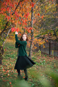 红头发的女孩在充满五颜六色的叶子的秋天花园里跳舞和玩耍。