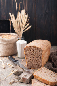 全麦面包。 无酵小麦面包在砧板上，面粉麦粒小穗在木制棕色桌子上。 一条切成碎片的面包。 复制空间。 黑暗的背景。 自制的。