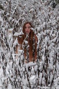 年轻的女人留着长发在冬天霜冻寒冷的健康后，桑拿使冰在雪覆盖的灌木丛。