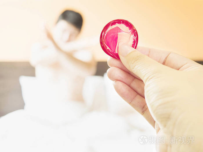 女人拿着红色避孕套,背景模糊,男人在床上做反或拒绝行动