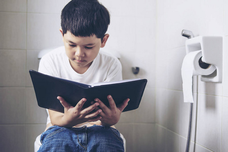亚洲男孩坐在马桶边看书,健康问题的概念照片