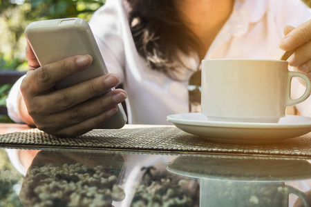 女士在喝咖啡时使用手机的裁剪图像