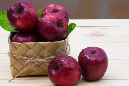 放在木桌上的糖掌叶子编织容器里的带水滴的新鲜苹果