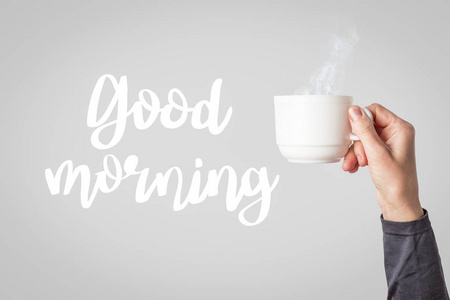 女性穿着衣服，拿着一个白色的杯子，在浅灰色的背景下喝热咖啡或茶。 添加文本早上好。 早餐概念与热咖啡或茶。