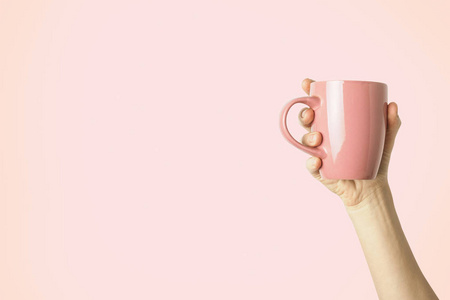 女性手拿着一个紫色的杯子，上面有热咖啡或茶，背景是浅粉色的。 早餐概念与热咖啡或茶。
