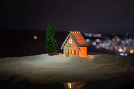 圣诞节和新年的微型房子在雪中与杉树。 雪地上的小玩具屋，背景上有树和博克城的灯。 圣诞装饰品。 假日概念。