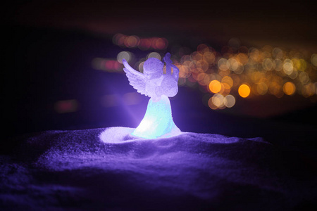 圣诞天使在模糊博克城灯在夜间背景。 白雪公主守护天使。 圣诞装饰