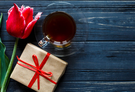 红色郁金香盒子，红色丝带和一杯咖啡在灰色的木桌上。 情人节春天的背景。 花卉模拟。 与共空间