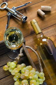 瓶子和一杯白葡萄酒，葡萄，软木塞和木底上的开瓶器。 上面的风景。