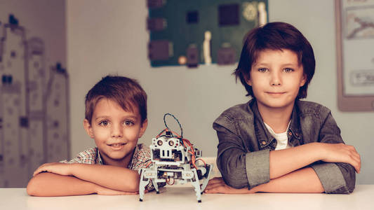 两个男孩坐在桌子旁，建造机器人。穿衬衫的男孩。室内欢乐。现代霍比概念。现代技术。机器人工程概念。带着罗伯的少年。为乐趣而创新。