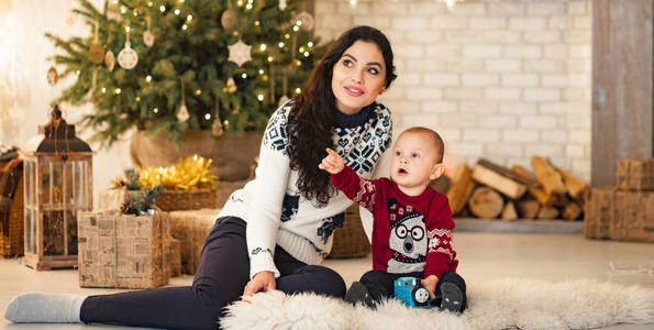 母亲和她的儿子坐在地毯上，在圣诞树和礼品盒的背景下玩耍。