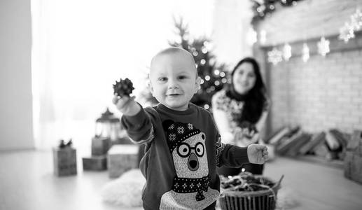 小男孩正在圣诞树节日花环和礼品盒的背景下玩耍。 黑白图像。
