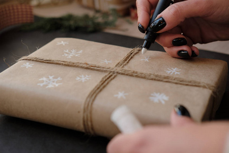 女人在纸包上画雪花，在黑色背景上画圣诞盒礼物。 女手在寒假礼物上画画。 圣诞节新年购物准备假日概念