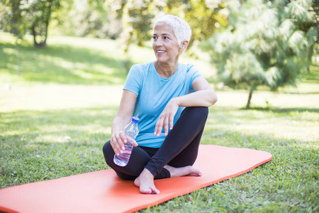 一位资深运动妇女坐在外面的垫子上，锻炼后休息
