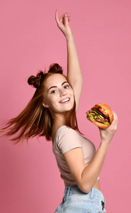时尚和年轻的女孩戴着太阳镜拿着汉堡在粉红色的背景