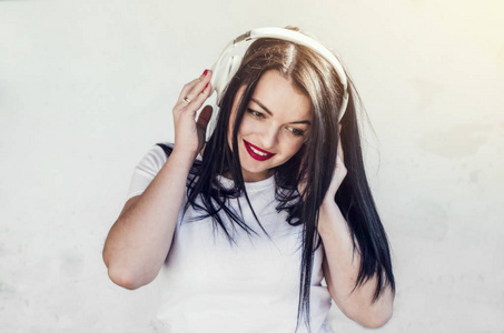 美丽的微笑黑发女孩听平静的音乐在白色无线耳机。 现代技术娱乐。