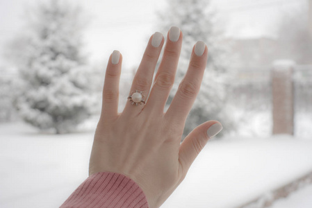 你好，冬天 女性的手欢迎她家院子里的第一场雪，背景是白雪覆盖的铲子和一个树篱。