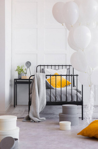 毛毯和橙色枕头在床旁边的桌子与植物在卧室内部与气球。真实照片
