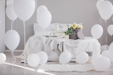 床上的花带毯子和枕头，在灰色的卧室内部，白色的气球。 真实照片