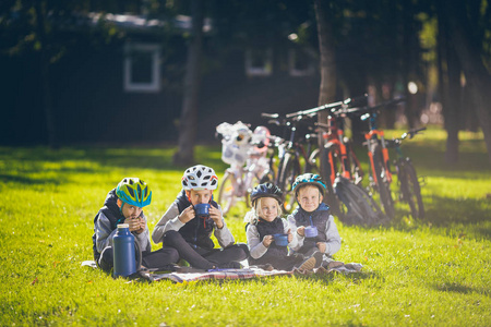 主题活跃家庭假日性质。 成群的人，小孩子，三个兄弟姐妹，坐在自行车旁，在公园的绿草草坪上休息，喝杯子和热水瓶茶。