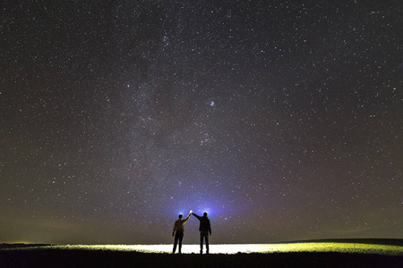 手持扑克牌打牌摄影图在美丽的深蓝色夏季星空下,两个手持手电筒的人