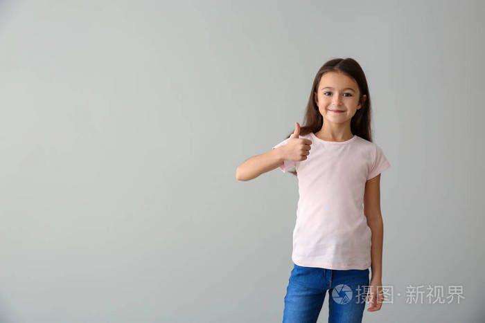 穿T恤的可爱女孩在浅色背景上露出拇指