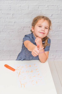 一个坐在桌子旁的女孩在一张纸上画着白色砖墙