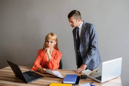 一位商务女性和男性在一个木制的办公桌上工作，在纸和电脑上灰色背景