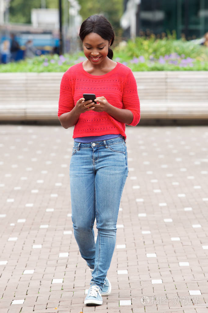 城市中带着手机走路的年轻黑人微笑的完整画像