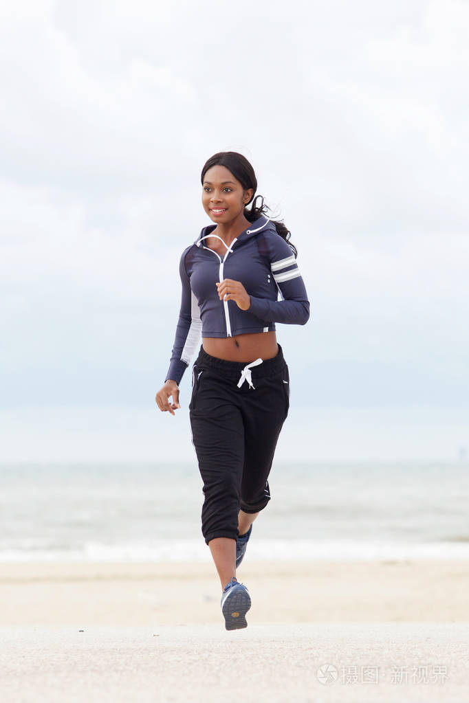 健康的年轻黑人妇女在海滩上奔跑的全身正面肖像