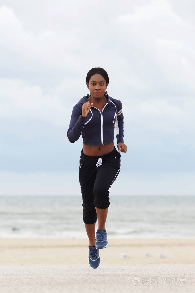 在海滩上奔跑的年轻黑人女子的全身正面肖像