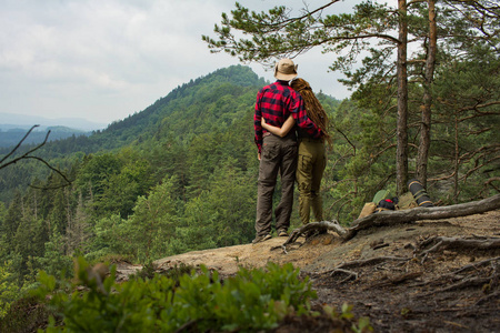 两个旅行者站在悬崖上，观看美丽的山脉和森林