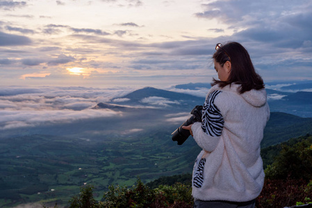 女游客在泰国卢埃省国家公园日出背景下拍摄太阳雾和山的自然景观后，正在观看摄像机。