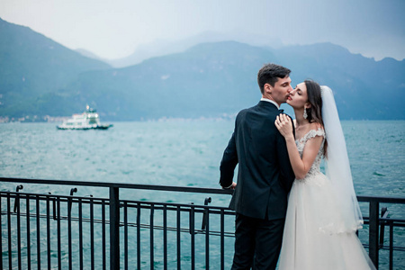 一对新婚夫妇在阴天的湖和山的背景下接吻