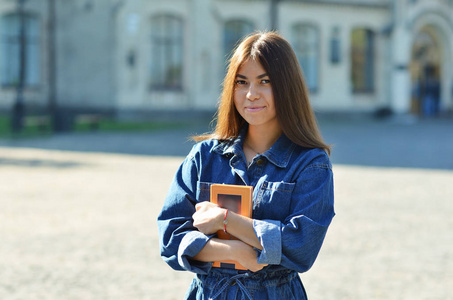 快乐可爱的年轻女子学生拿着书在户外散步