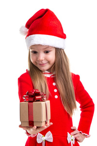 微笑的圣诞女孩看着礼物, 手里拿着它, 戴着一顶圣诞老人的帽子, 在白色的背景隔离