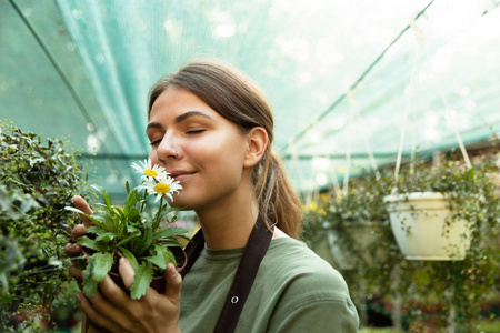 照片吸引人的可爱的女人园丁闻着温室里的植物。