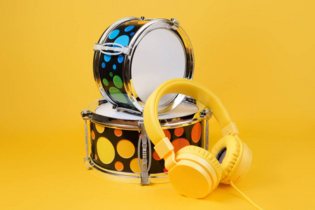 黄色耳机和迷你鼓套件在黄色的背景。玩具鼓