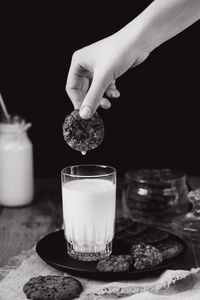 玻璃与新鲜牛奶和自制巧克力饼干在木制桌子上。 早餐。把巧克力饼干放进牛奶里