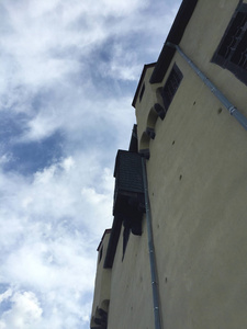 一座中世纪城堡的浅褐色墙壁上升成一片蓝天，白云。 唯一的窗户在屋顶附近。 从墙上伸出的厕所或垃圾箱。