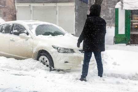 汽车在城市街道上被积雪堵塞了。 在大雪暴风雪和风暴中，人们用刷子清洗雪中的车辆。 冬天的天气预报。